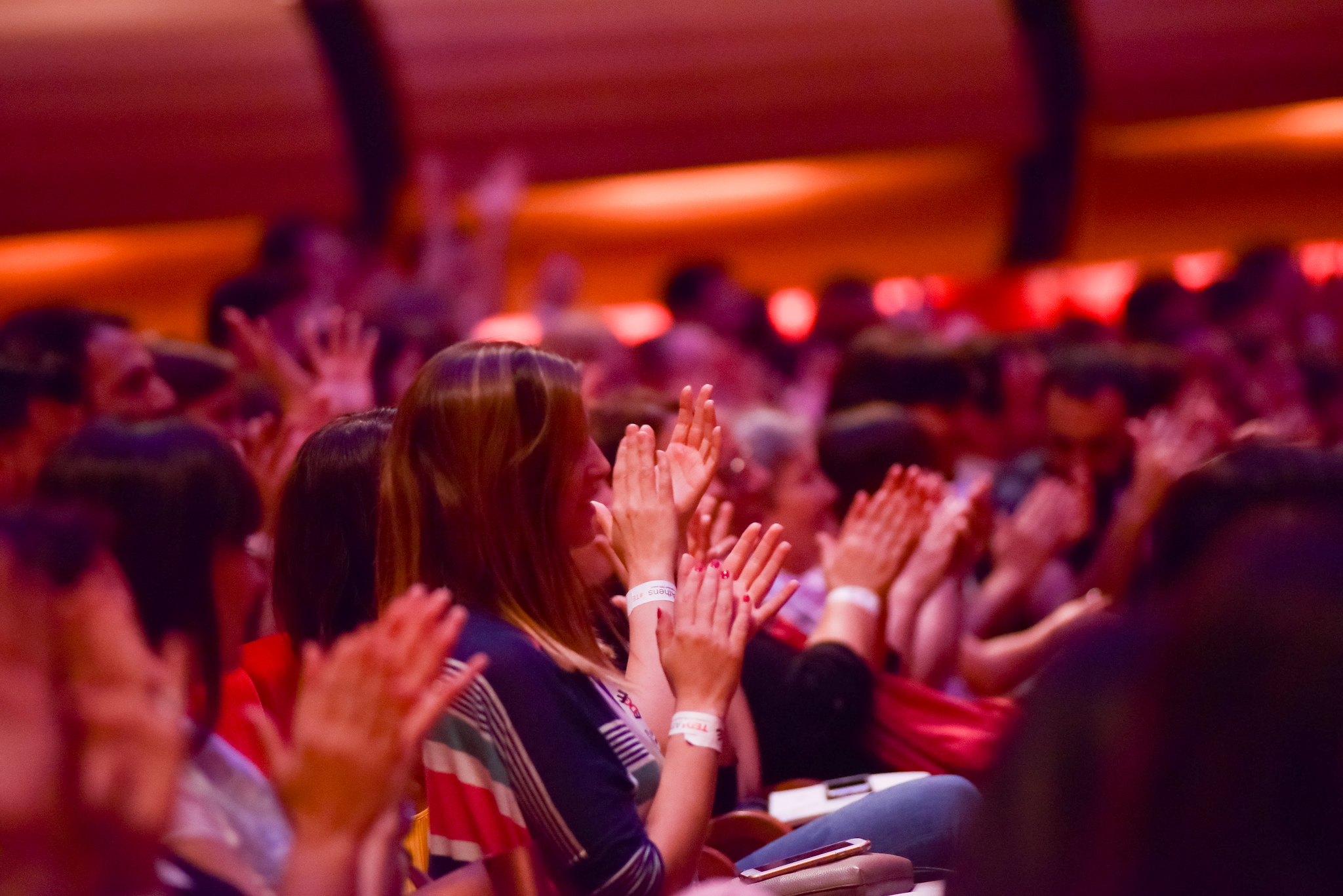 Audience mid-applause, hands raised, warm house light