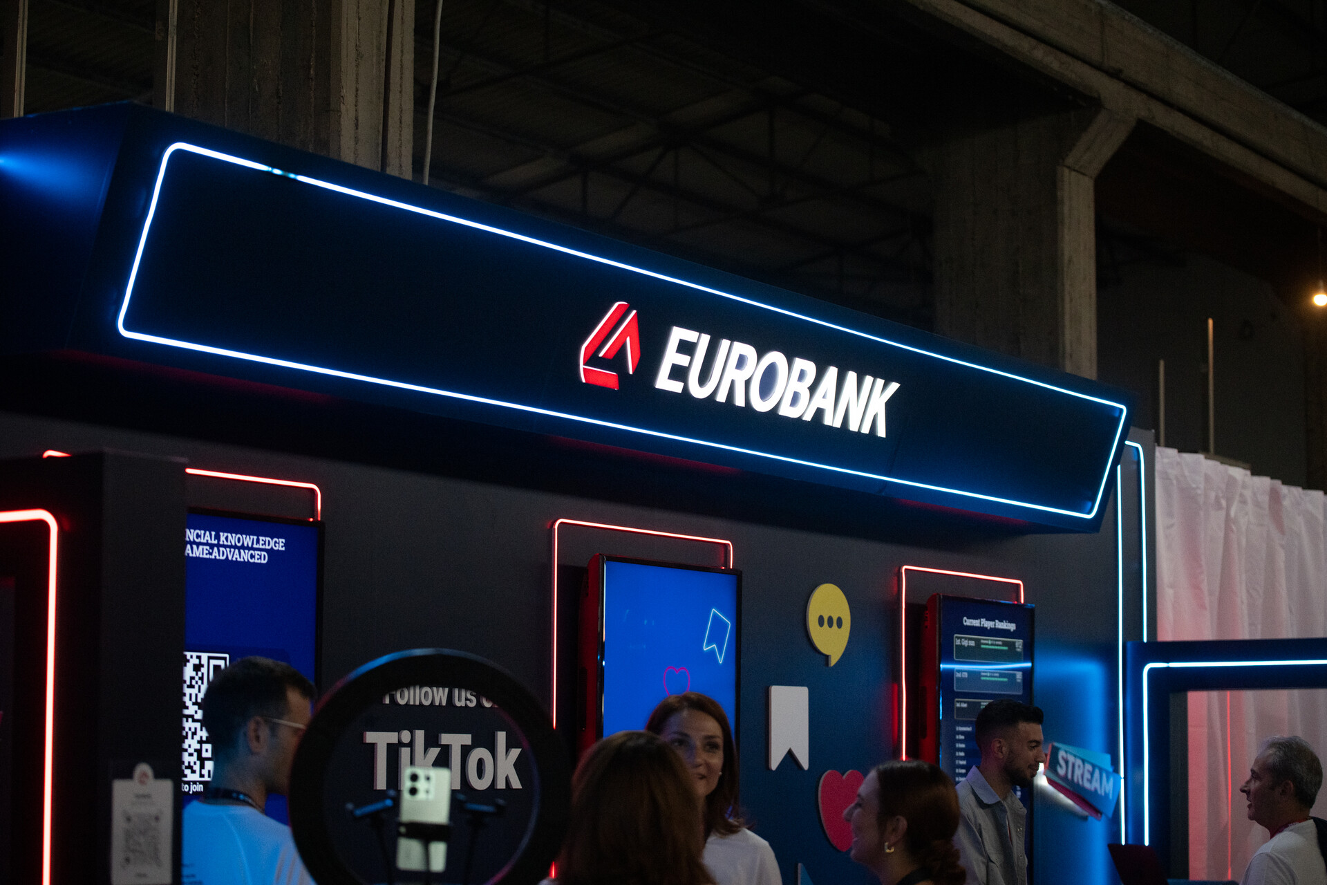 The lit Eurobank sign above the studio, crowd below