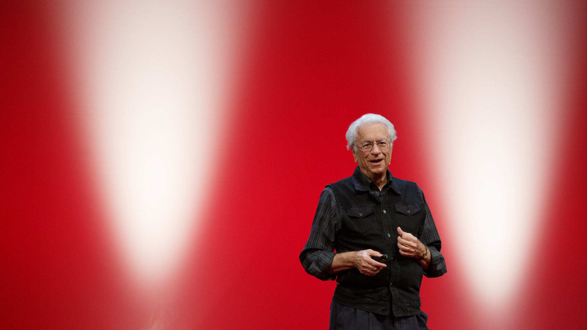 Speaker mid-talk against a lit red stage wall